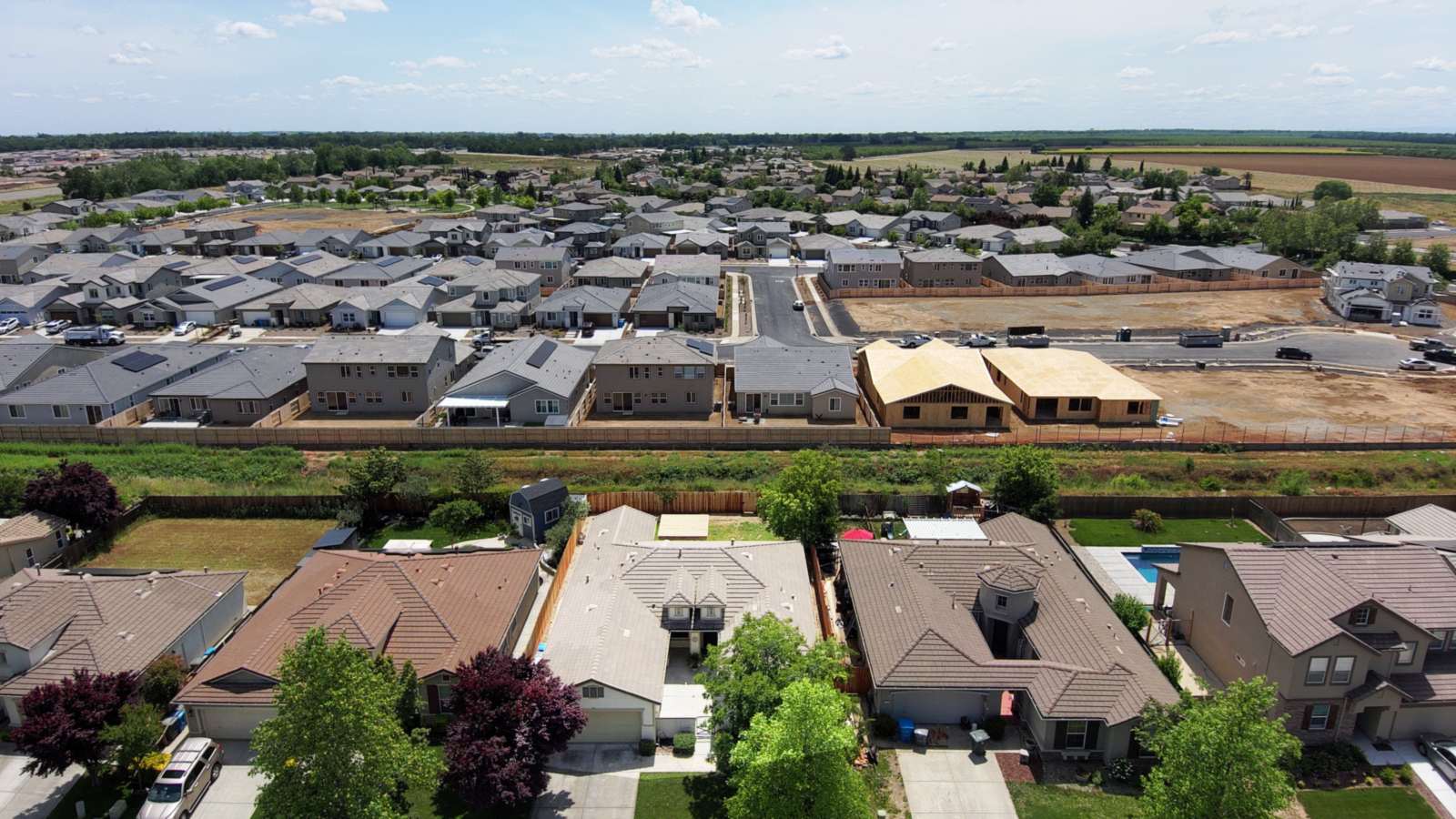Aerial view of a residential subdivision with finished homes, two houses in wood framing, and graded vacant lots