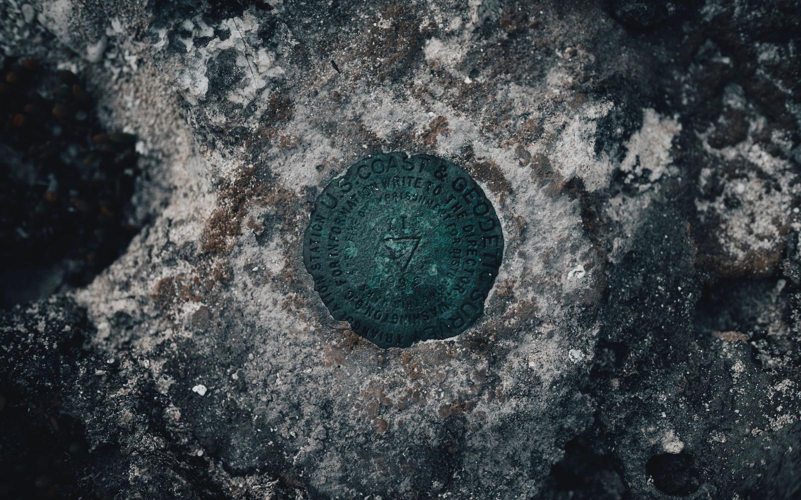 Close-up of a weathered bronze U.S. Coast & Geodetic Survey triangulation station disk, green with age and stamped with a triangle and the year 1932, set in gray rock