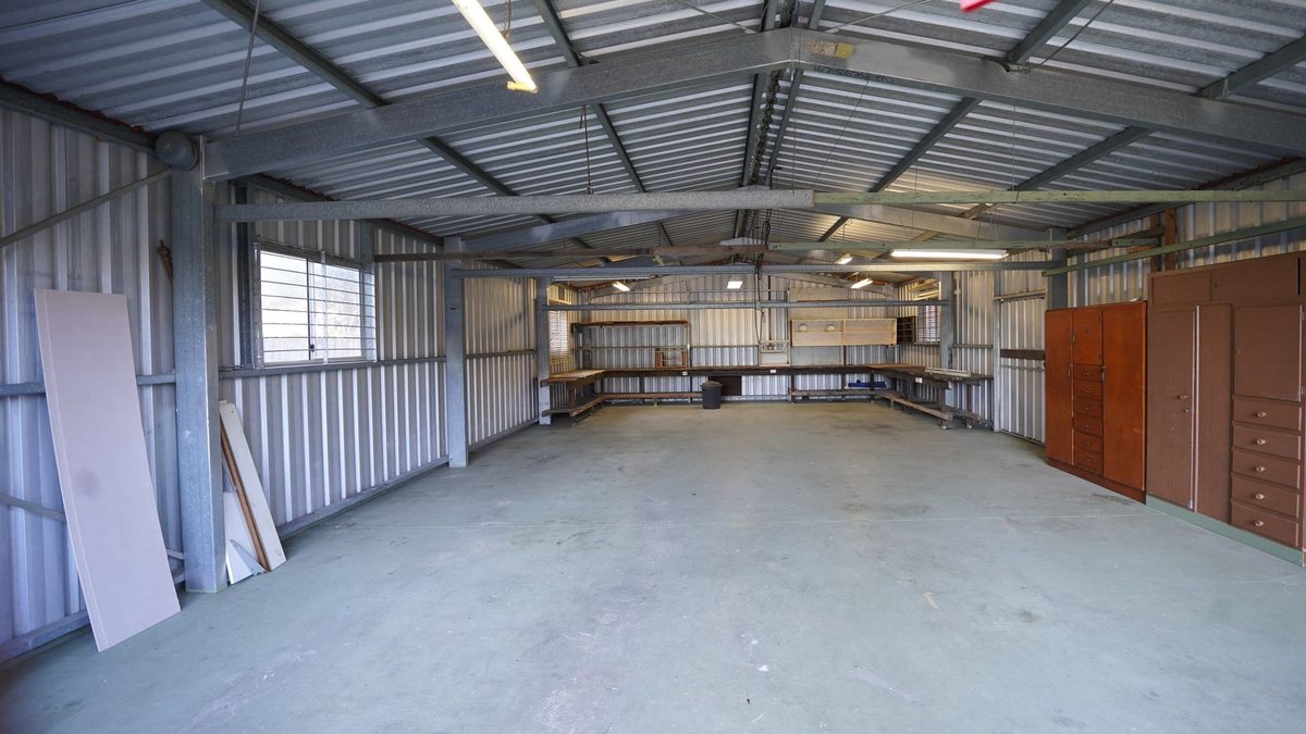 Interior of an empty steel-framed shop building, with gray steel columns and gable roof frames, corrugated metal roof and wall panels, a concrete floor, workbenches along the back wall and brown cabinets on the right