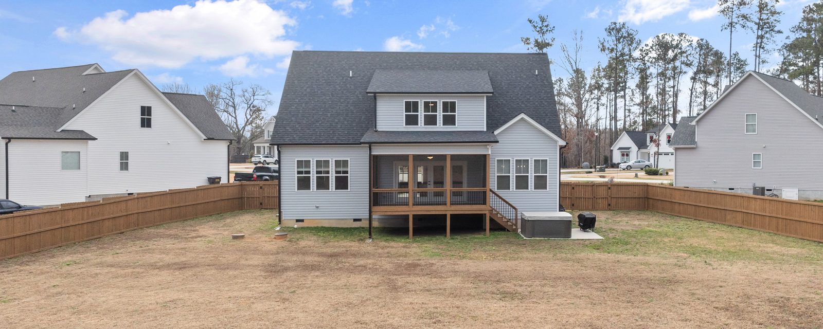 Wood privacy fences run along both sides of a large grassy backyard behind a new two-story suburban house with a screened porch, with neighboring houses beyond the fences.