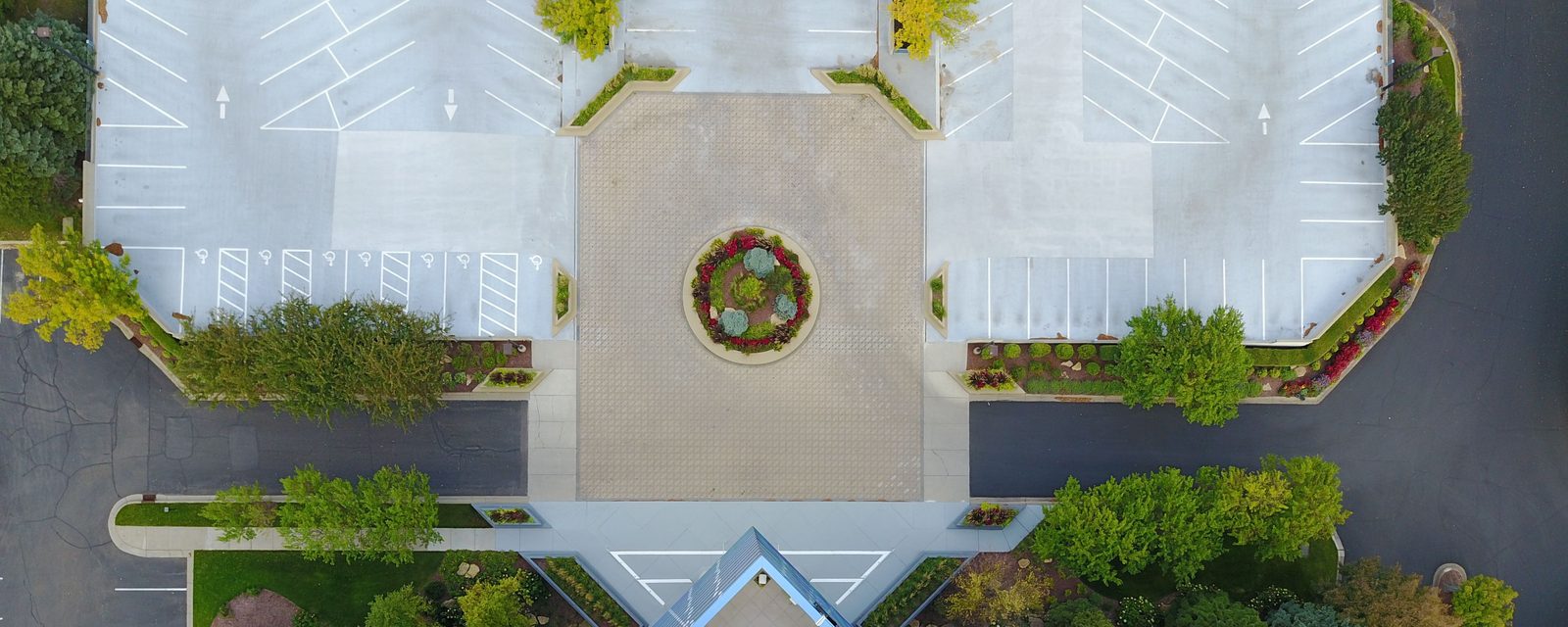 Top-down aerial view of a building entrance, entry plaza and striped parking lots with accessible stalls, drive aisles and landscaped islands.