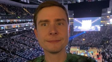 Nicholas Quedens in a green tie-dye shirt, taking a photo inside an indoor sports arena